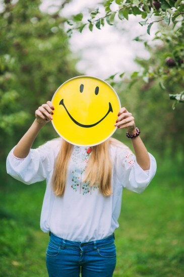 A Woman covering her face with a smiley card